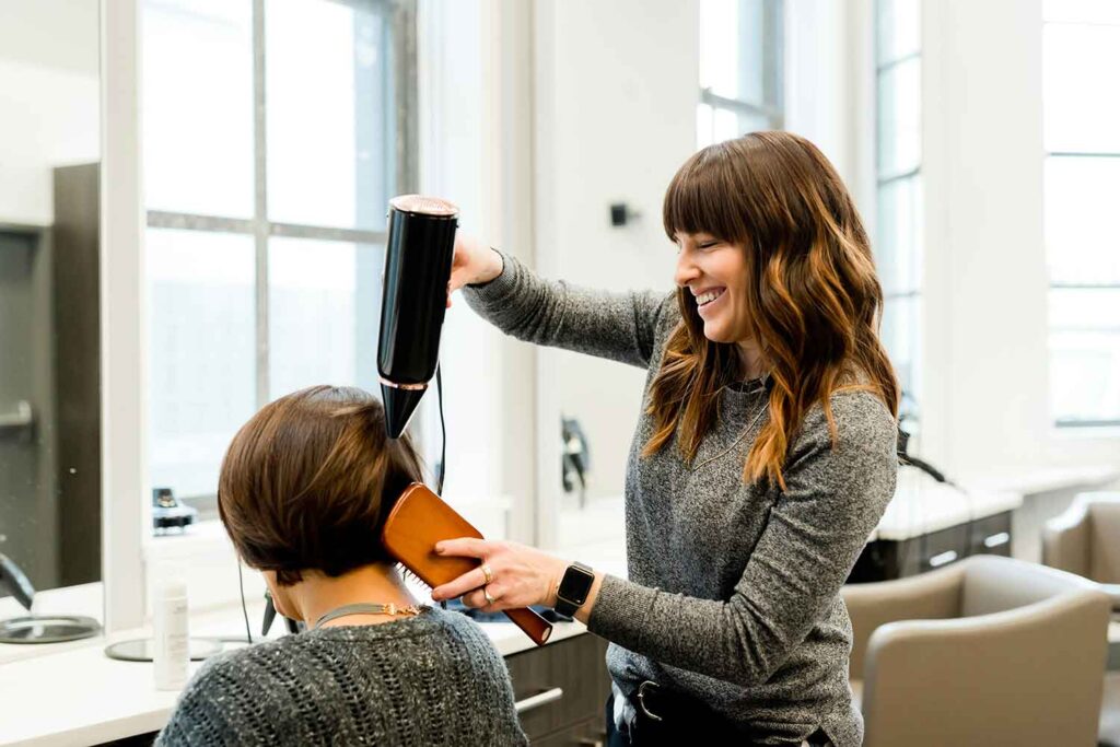 Hairstylist smiling while blow-drying a client’s hair inside a bright Bay Area salon
