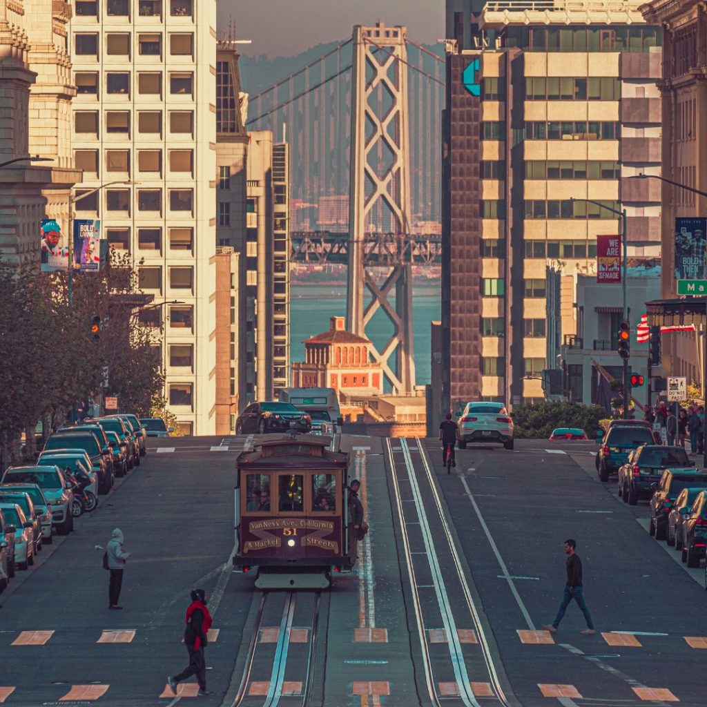 San Francisco street with cable car and Bay Bridge visible between downtown buildings.