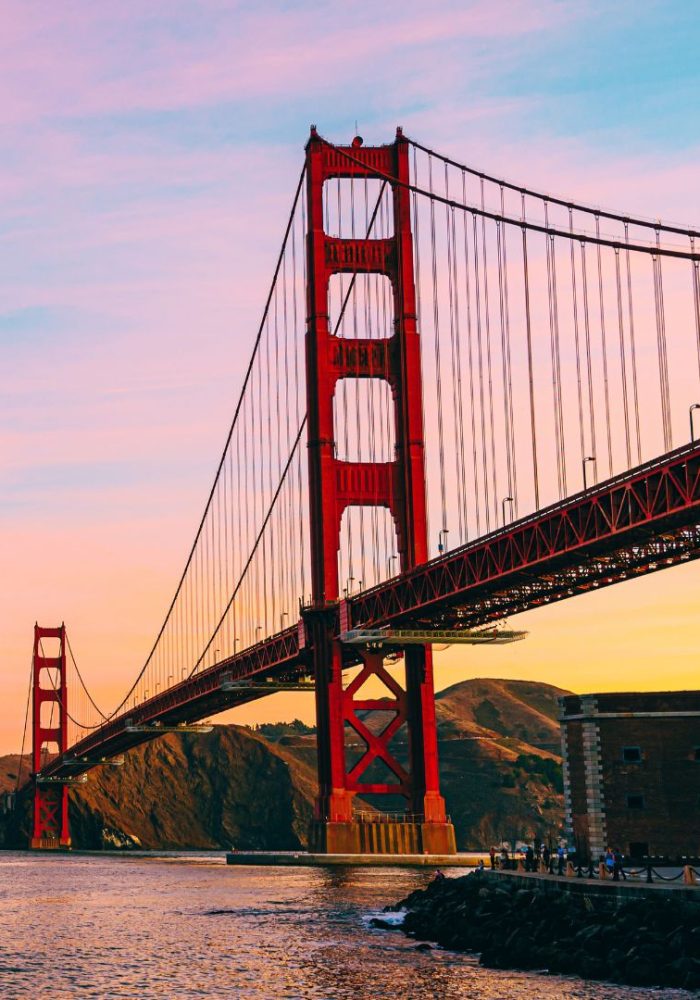 Golden Gate Bridge in San Francisco at sunset, with the red suspension bridge spanning over water and hills in the background.