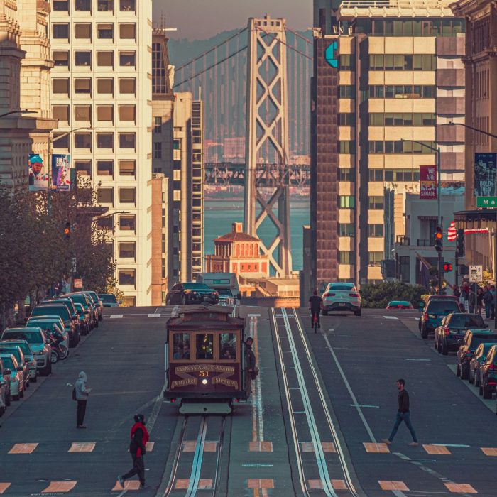 San Francisco street with cable car and Bay Bridge visible between downtown buildings.